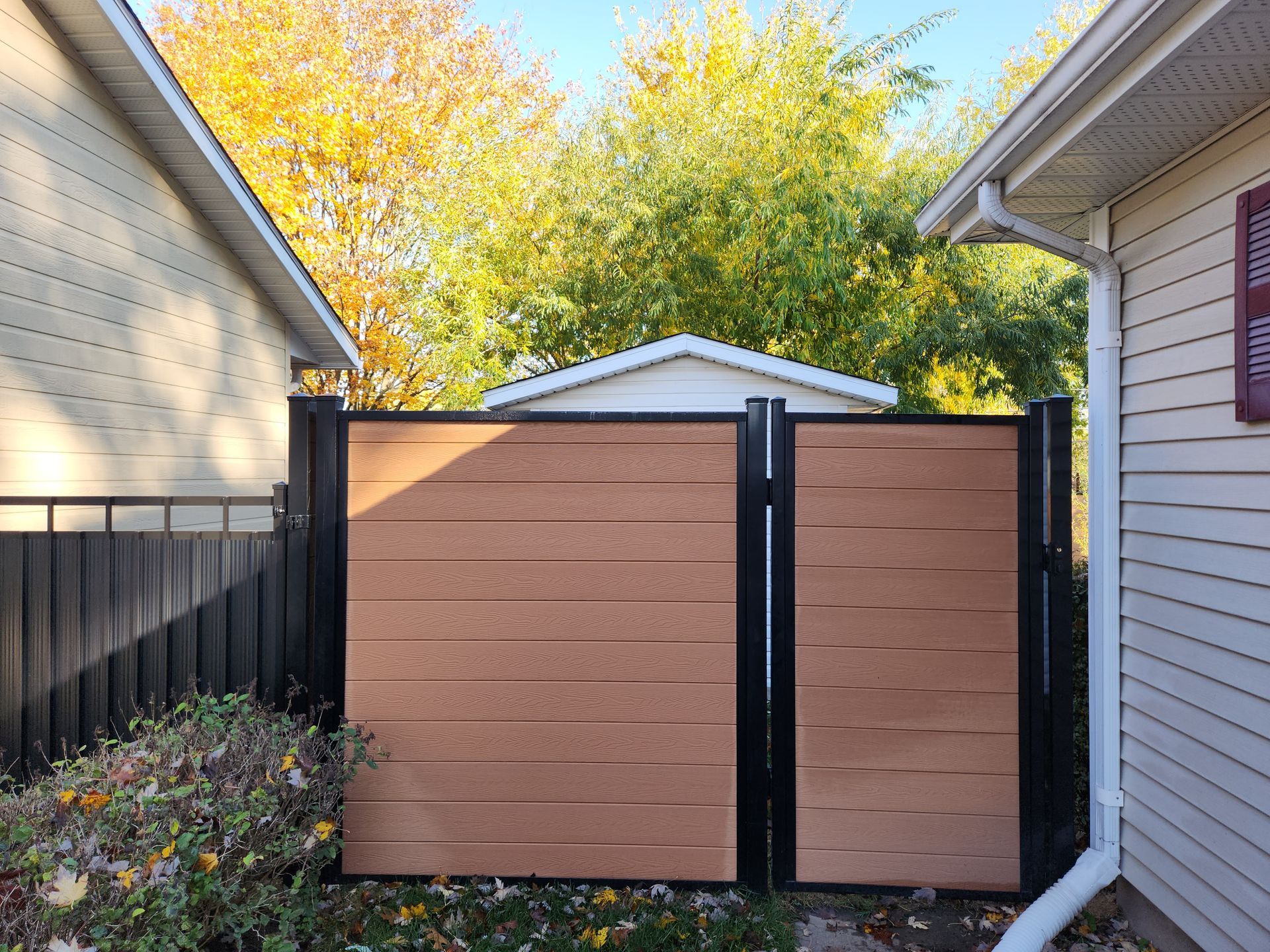 Une clГґture en bois avec un portail noir se trouve entre deux maisons.