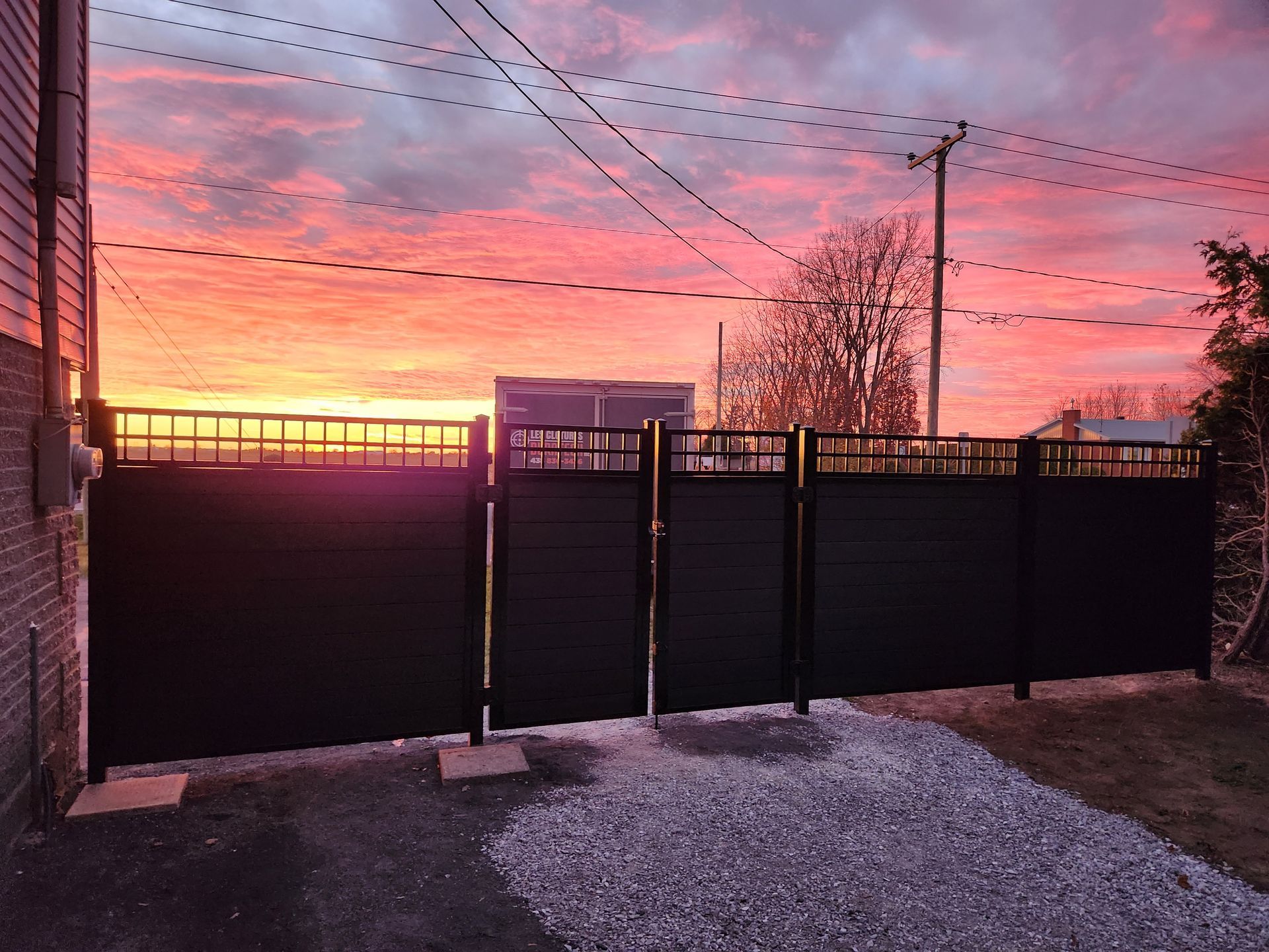 Une clГґture noire avec un coucher de soleil en arriГЁre-plan.