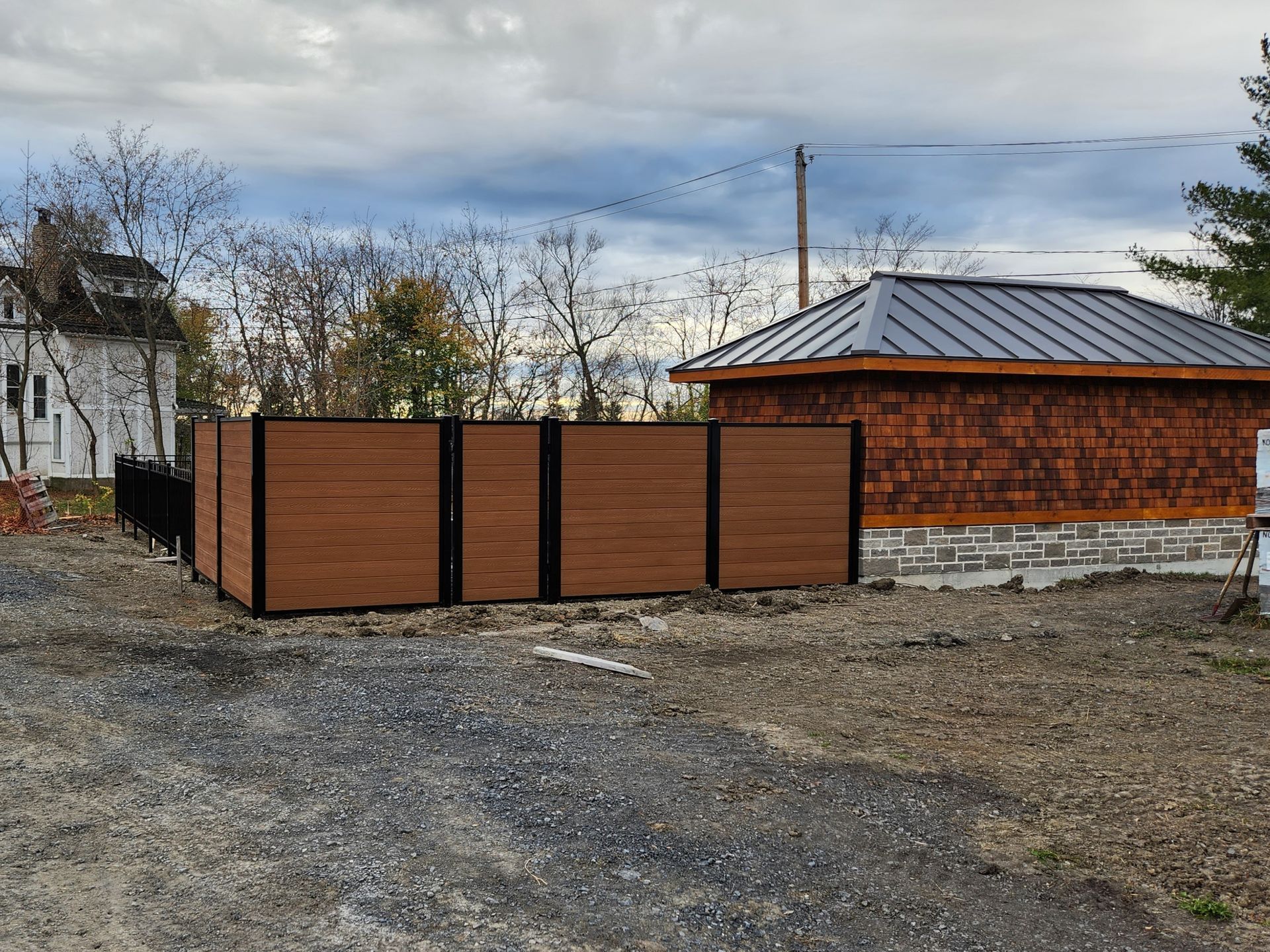 Une clГґture en bois se trouve devant un bГўtiment avec un toit en mГ©tal.