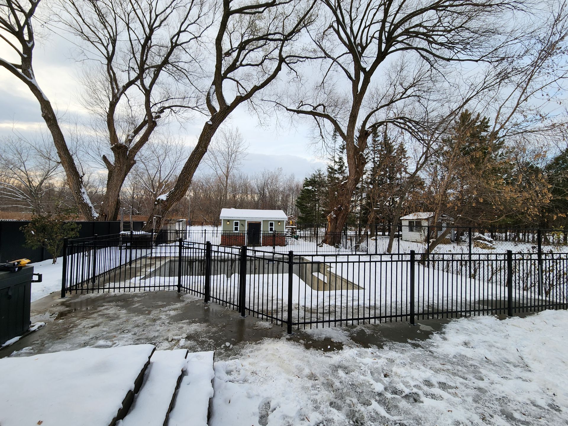 Une cour enneigГ©e avec une clГґture et des arbres en arriГЁre-plan.