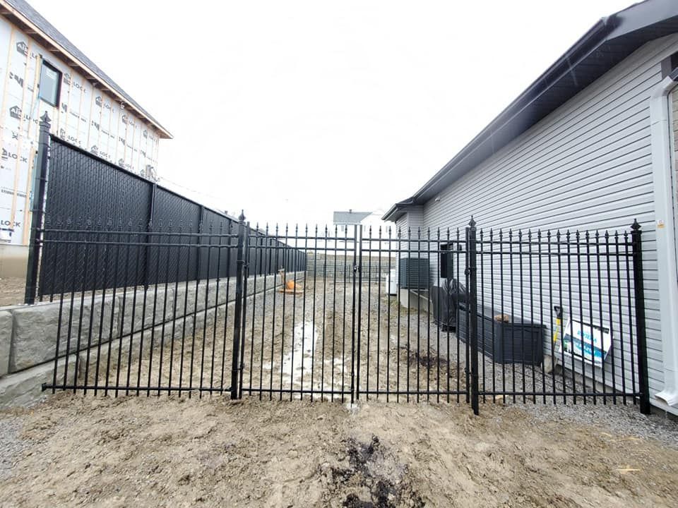 Une clГґture mГ©tallique entoure une cour en terre devant une maison en construction.