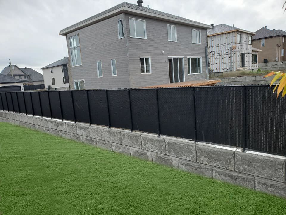 Une clГґture grillagГ©e noire entoure un mur de briques devant une maison.