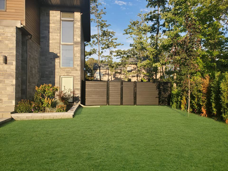 Une grande pelouse devant une maison avec une clГґture et des arbres.