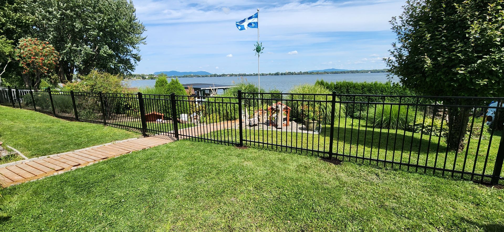 Une clГґture entoure un champ verdoyant avec vue sur un lac.