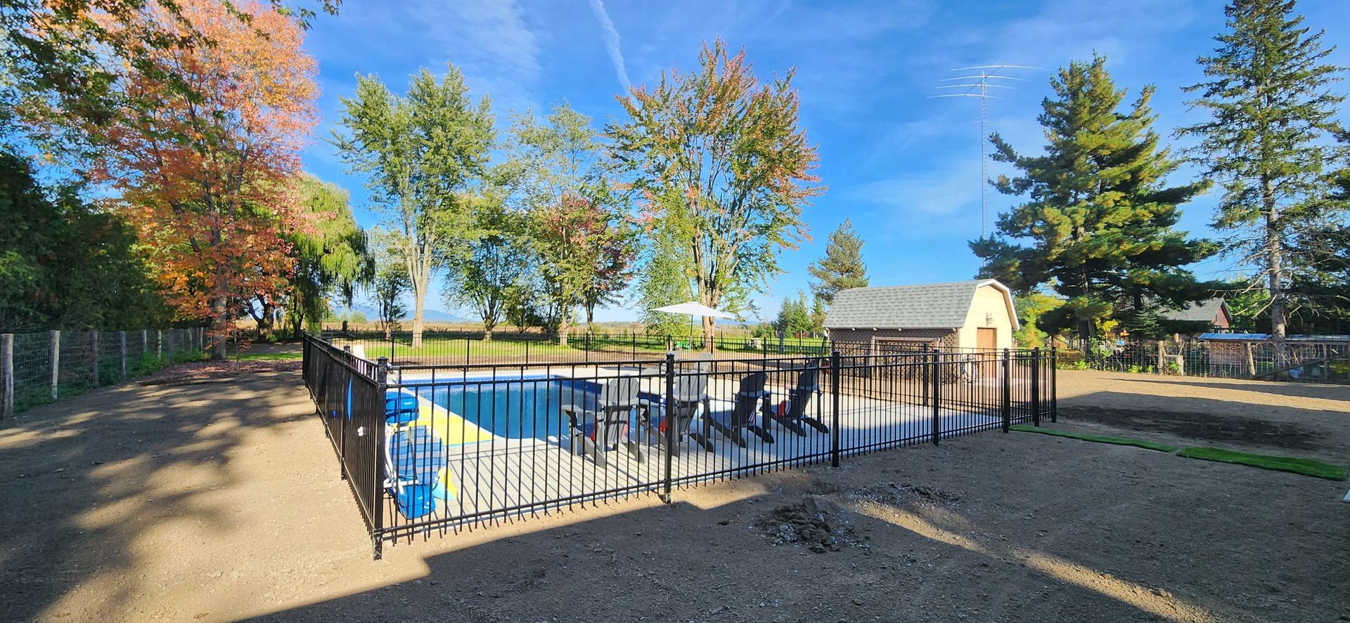 Une grande piscine entourГ©e d'une clГґture et d'arbres par une journГ©e ensoleillГ©e.