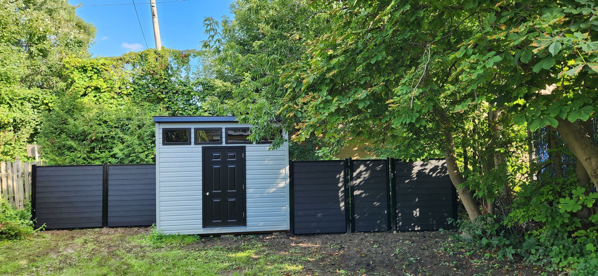 Un petit hangar blanc se trouve au milieu d'une cour entourГ©e d'arbres.