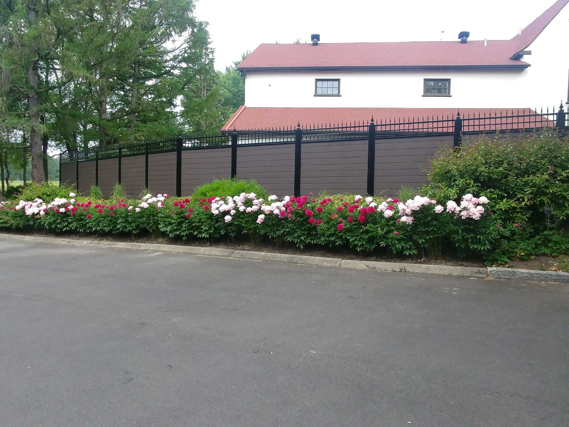 Une maison avec un toit rouge se trouve derriГЁre une clГґture avec des fleurs devant elle.