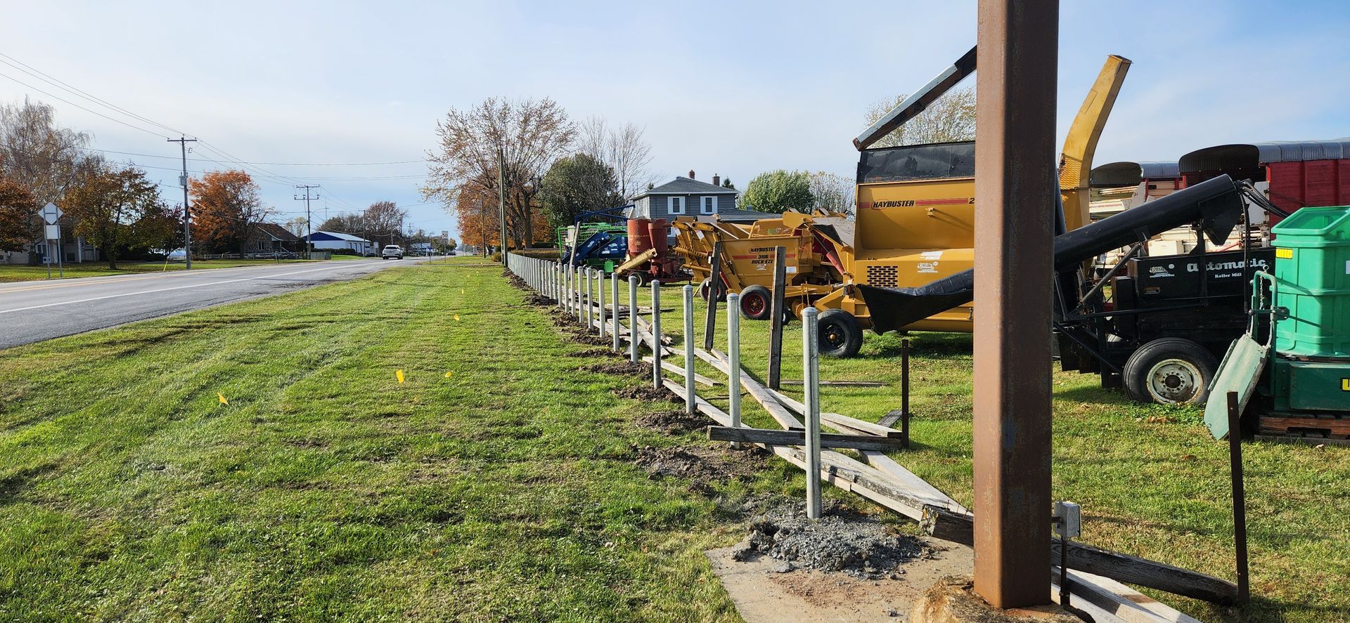 Une clГґture est en cours de construction Г  cГґtГ© d'une route dans un champ herbeux.